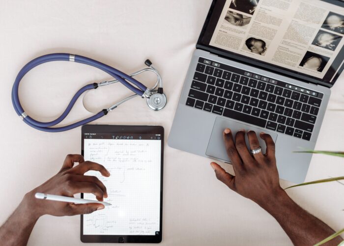 Innovation in the NHS A doctor using a tablet and laptop with a stethescope on their desk